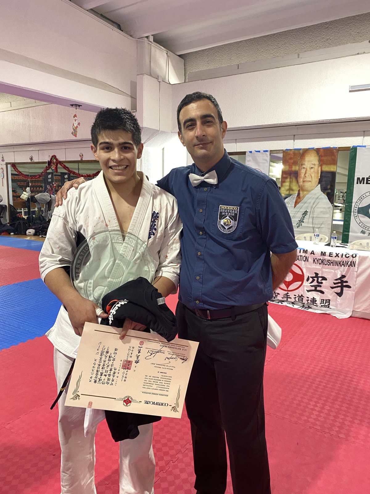 Eduardo Gómez Quiroga con el diploma y el trofeo de la prueba de 30 kumites, junto a un oficial de IKO Matsushima México